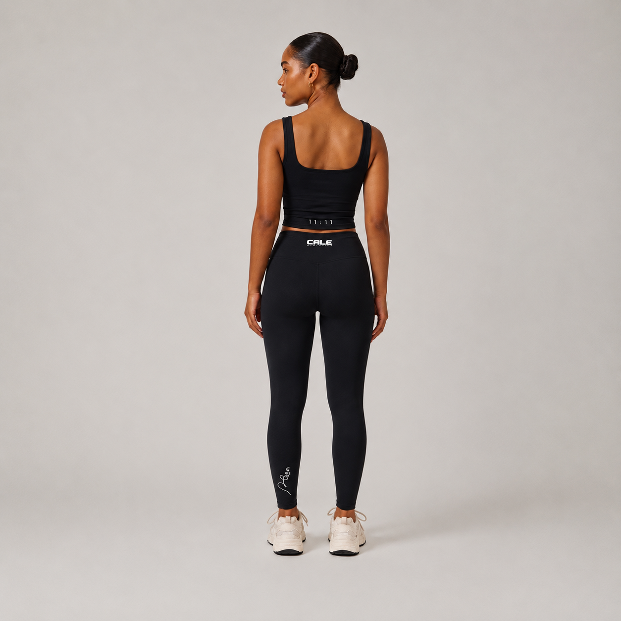 Black fitted tank top worn by a model, styled with wide straps and paired with black leggings against a neutral background.