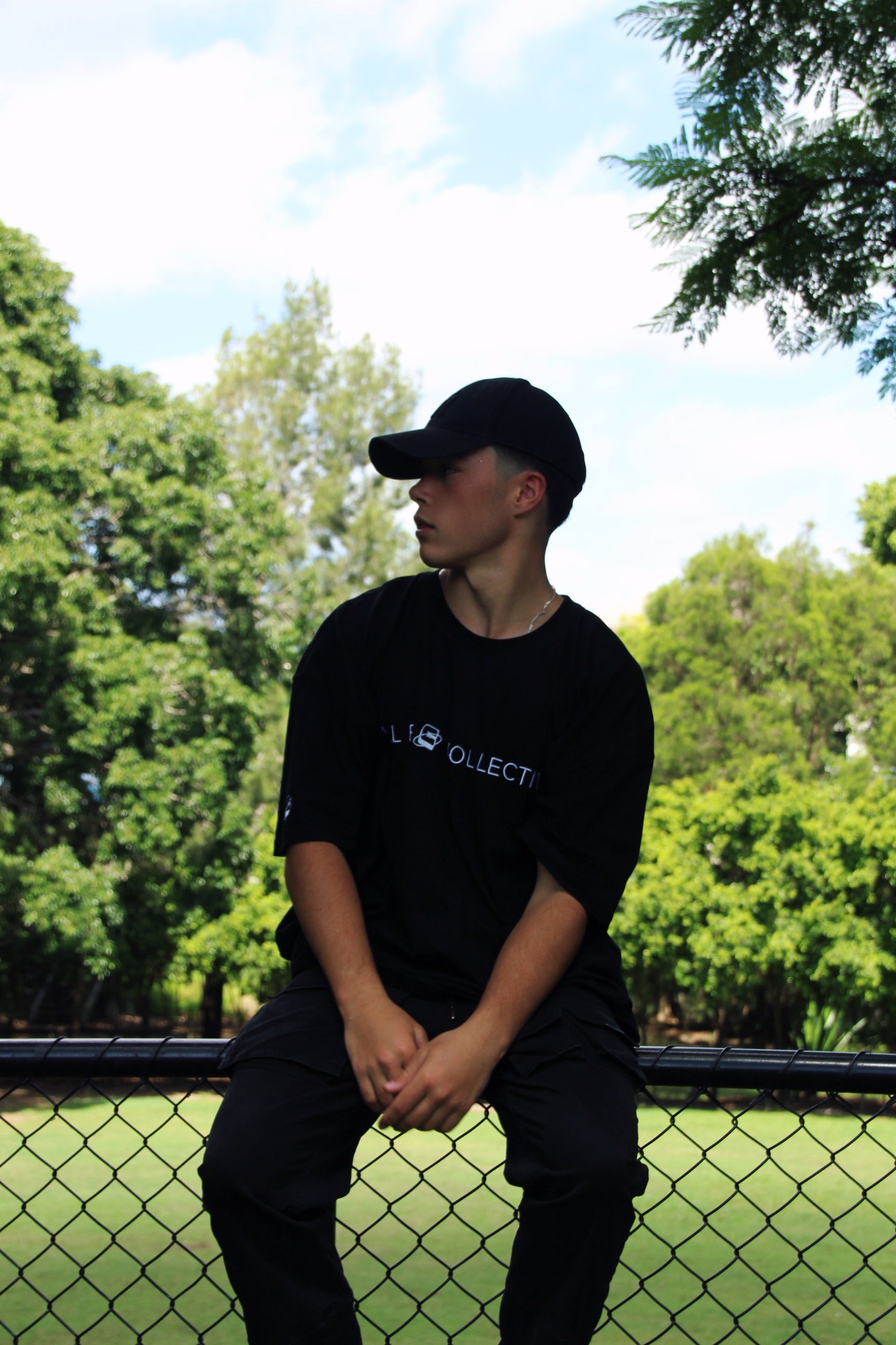 Person seated outdoors wearing a black oversized graphic t-shirt with a visible design, showcasing a relaxed fit.