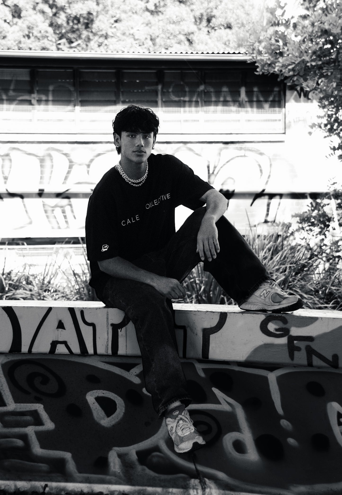 Person wearing a black oversized graphic t-shirt with 'CALE COLLECTIVE' text in an urban setting.