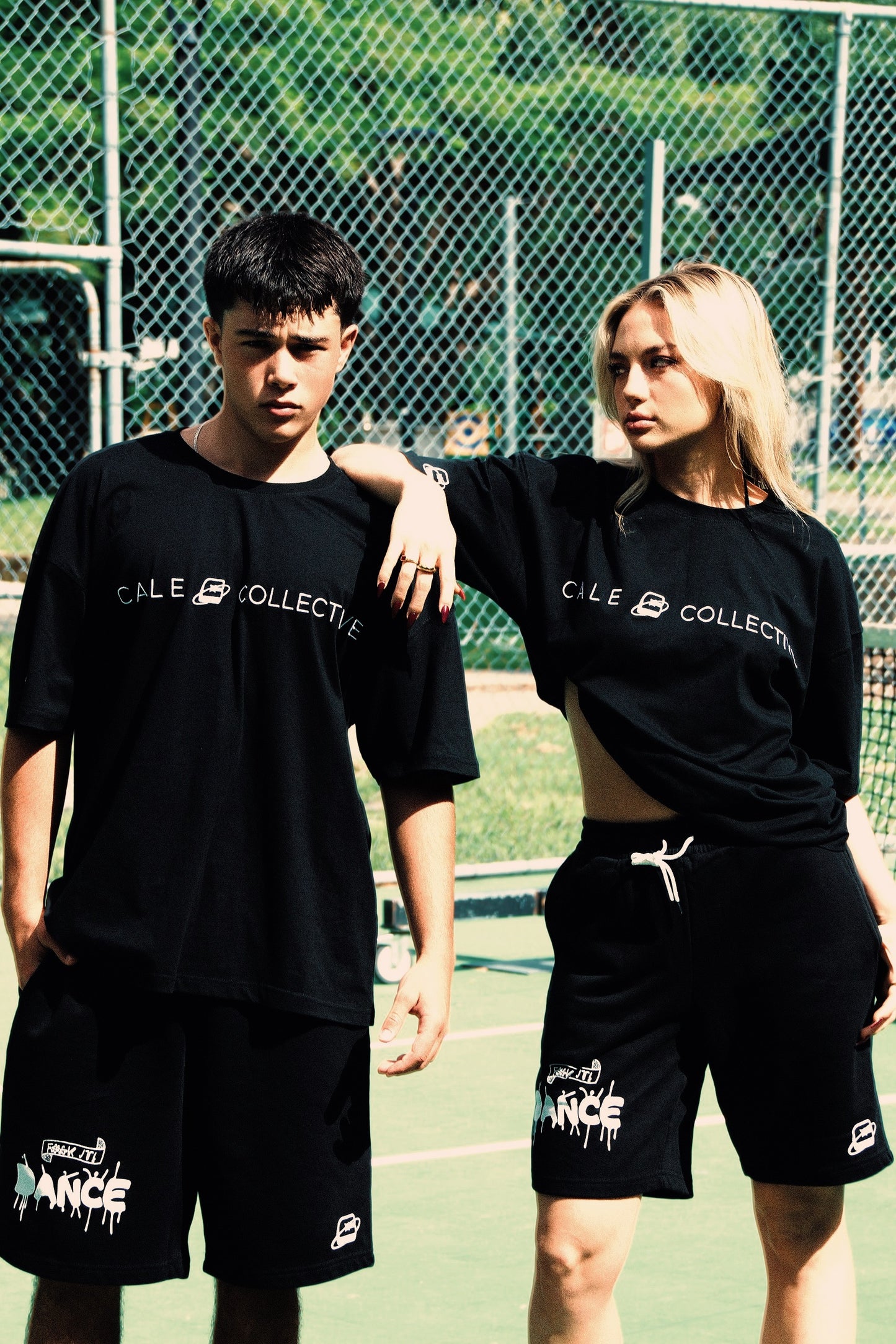 Two individuals wearing black oversized graphic t-shirts styled with casual shorts on a sports court.