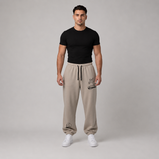Person wearing stone oversized track pants with elastic waistband and drawcord, styled with a fitted black t-shirt and white sneakers.