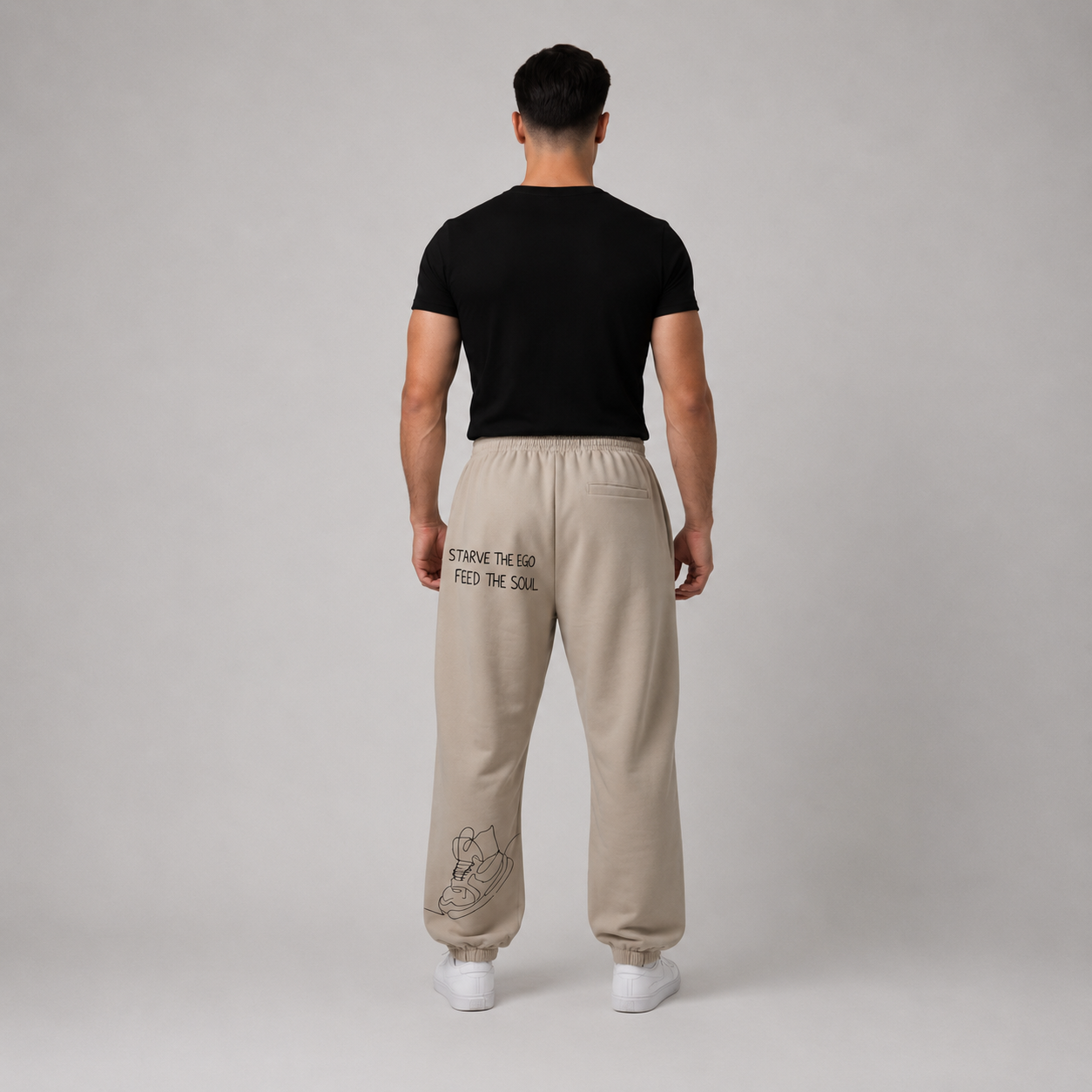 Person wearing stone oversized track pants with an elastic waistband and graphic design on the back, paired with a black t-shirt.